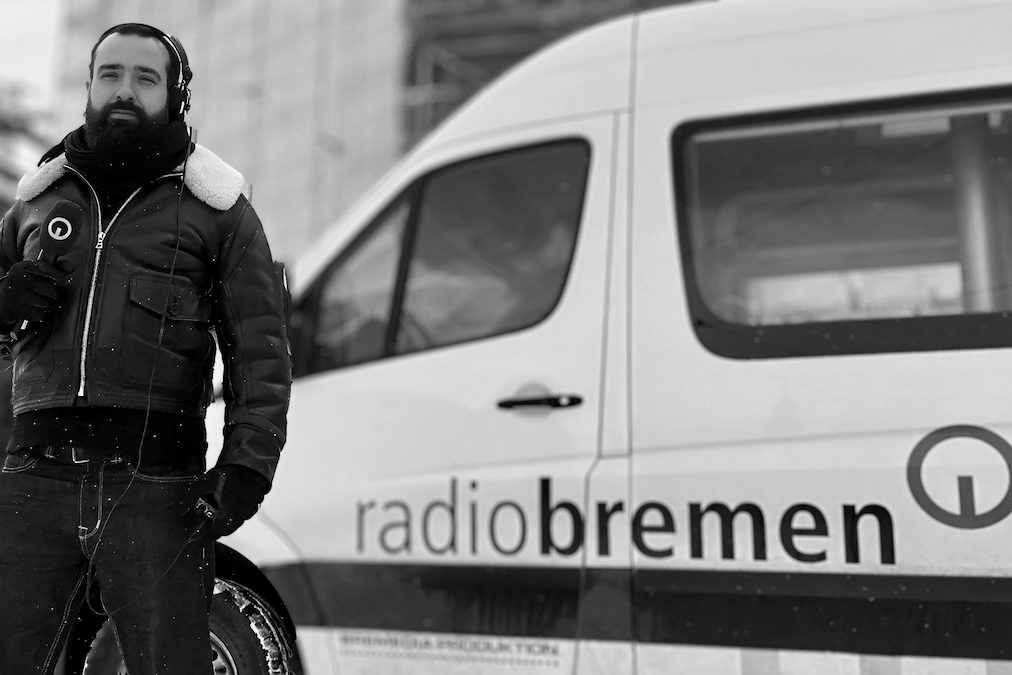 Justus Wilhelm mit Kopfhörern neben einem Übertragungswagen von Radio Bremen.