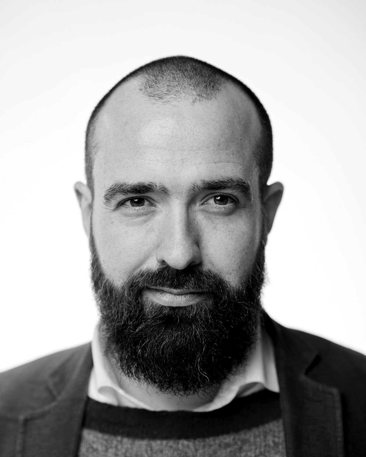 Porträt von Justus Wilhelm: Vollbart, Sakko über Pullover, Blick in die Kamera.